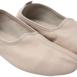Pu&ograve; includere: Un paio di ballerine in pelle beige chiaro. Le scarpe hanno la punta arrotondata e una cucitura cucita al centro. I bordi sono rifiniti con un colore beige pi&ugrave; chiaro. Le scarpe sono progettate per il comfort e la flessibilit&agrave;.