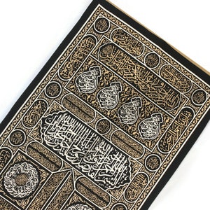 May include: Black fabric with gold and white Arabic calligraphy in a repeating pattern. The design features intricate details and a traditional Islamic motif.