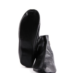 Puede incluir: Botines de cuero negro con cierre de cremallera. Una bota est&aacute; de pie, y la otra est&aacute; plana, mostrando la suela. Los botines tienen un dise&ntilde;o elegante y minimalista.