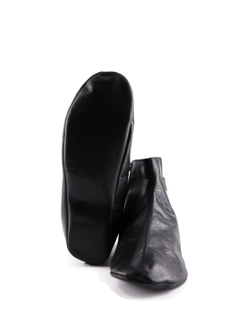 Puede incluir: Botines de cuero negro con cierre de cremallera. Una bota est&aacute; de pie, y la otra est&aacute; plana, mostrando la suela. Los botines tienen un dise&ntilde;o elegante y minimalista.