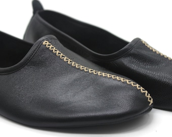 Puede incluir: Un par de zapatos negros de cuero sin cordones con un detalle de costura decorativo de color beige claro.