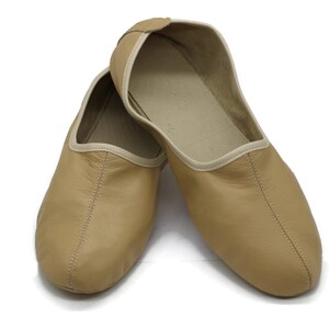 May include: A pair of tan leather slippers with a white trim. The slippers are pointed toe and have a simple design.