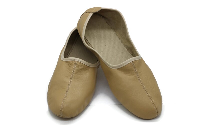 May include: A pair of tan leather slippers with a white trim. The slippers are pointed toe and have a simple design.