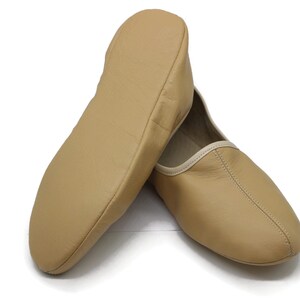 May include: A pair of tan leather slippers with a white trim. The slippers are made of soft leather and have a comfortable fit.