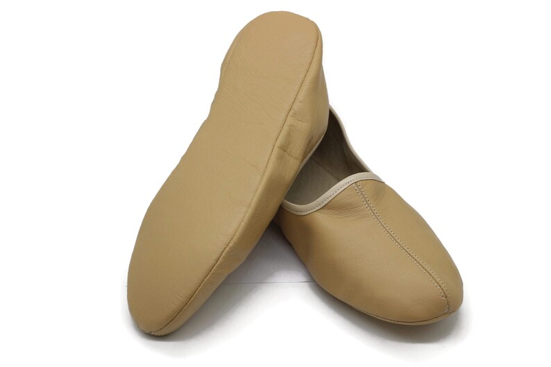 May include: A pair of tan leather slippers with a white trim. The slippers are made of soft leather and have a comfortable fit.