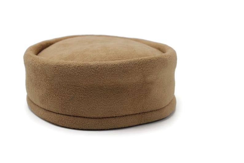 May include: A tan fleece hat with a rounded crown and a flat, circular brim. The hat is a solid color and appears to be made of a soft, textured material. The hat is a neutral color and could be worn by anyone.