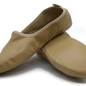 May include: A pair of tan leather ballet slippers with a light beige trim. The slippers are made of soft leather and have a comfortable fit.