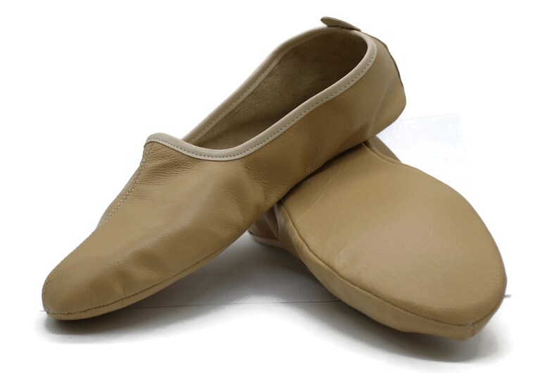 May include: A pair of tan leather ballet slippers with a light beige trim. The slippers are made of soft leather and have a comfortable fit.