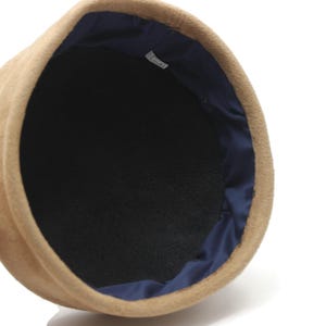 May include: A tan-colored hat with a dark blue interior lining. The hat has a rounded shape and a soft, textured appearance. The interior is black.