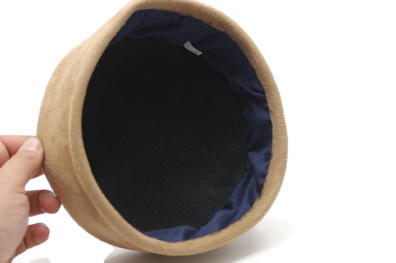 May include: A tan-colored hat with a dark blue interior lining. The hat has a rounded shape and a soft, textured appearance. The interior is black.