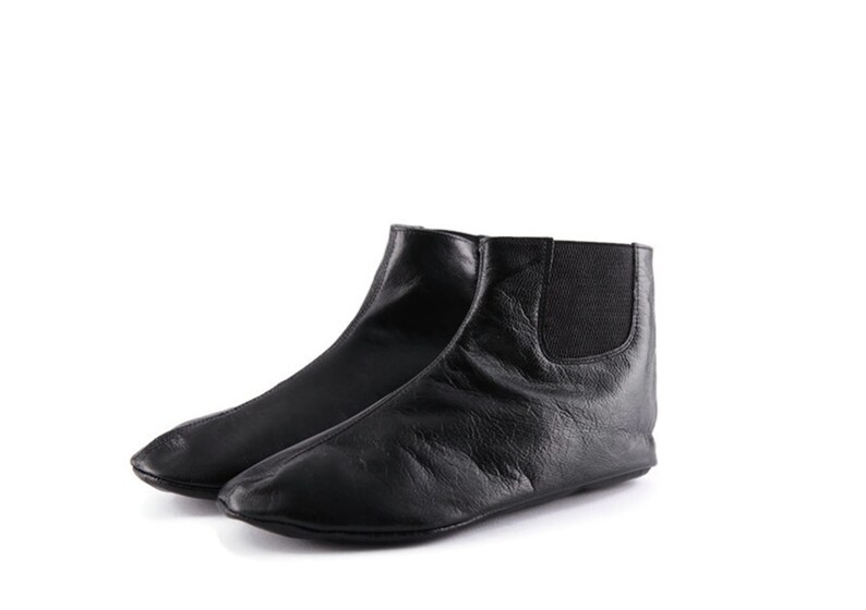 Puede incluir: Un par de botines de cuero negro. Una bota est&aacute; delante de la otra, mostrando el perfil lateral. Las botas tienen punta redondeada y paneles laterales el&aacute;sticos. Las botas son de cuero suave y texturizado.