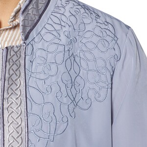 May include: A light blue long-sleeved shirt with a white collar and intricate embroidered details on the front. The embroidery features a geometric pattern in a lighter shade of blue.