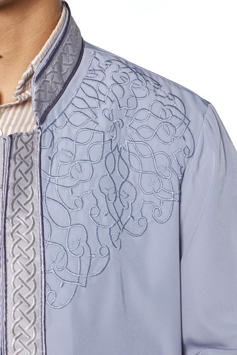 May include: A light blue long-sleeved shirt with a white collar and intricate embroidered details on the front. The embroidery features a geometric pattern in a lighter shade of blue.