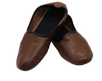Puede incluir: Un par de zapatillas de cuero marrón con ribetes negros. Las zapatillas están dobladas una sobre la otra.