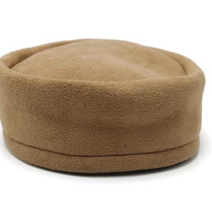 May include: A tan fleece hat with a rounded crown and a slightly raised brim. The hat is a solid color and appears soft and warm, suitable for cooler weather. The hat is a neutral color.