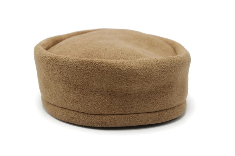May include: A tan fleece hat with a rounded crown and a slightly raised brim. The hat is a solid color and appears soft and warm, suitable for cooler weather. The hat is a neutral color.