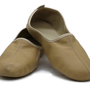 May include: A pair of tan leather slippers with a white trim. The slippers are made of soft leather and have a comfortable fit.