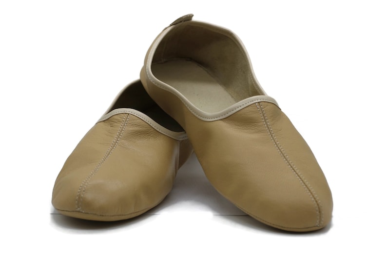 May include: A pair of tan leather slippers with a white trim. The slippers are made of soft leather and have a comfortable fit.