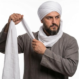 May include: A man wearing a white turban and a matching scarf, with a grey long-sleeved shirt. The man is holding the end of the scarf, with a neutral background.