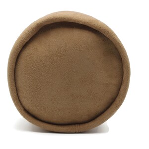 May include: A cylindrical, brown pillow with a soft, textured surface. The pillow has a rounded top and bottom, and a seam runs along the side. The neutral color and shape suggest a decorative or functional item for home decor.