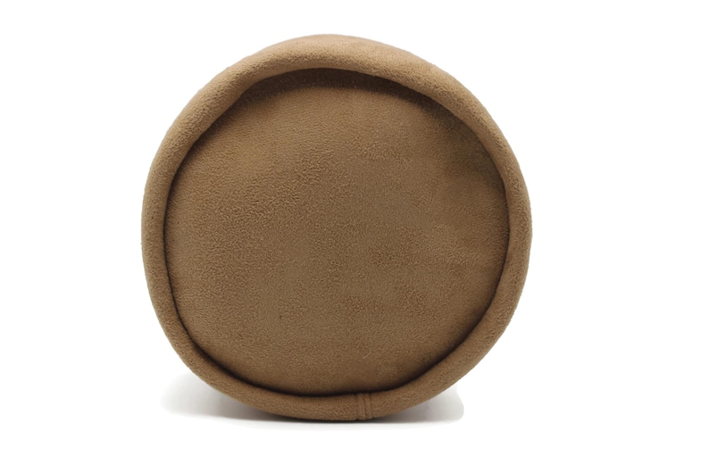 May include: A cylindrical, brown pillow with a soft, textured surface. The pillow has a rounded top and bottom, and a seam runs along the side. The neutral color and shape suggest a decorative or functional item for home decor.