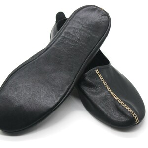 Puede incluir: Un par de zapatillas de cuero negro con un detalle de cadena dorada. Las zapatillas son suaves y c&oacute;modas, perfectas para relajarse en casa.