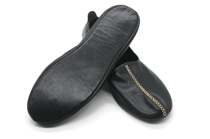 Puede incluir: Un par de zapatillas de cuero negro con un detalle de cadena dorada. Las zapatillas son suaves y c&oacute;modas, perfectas para relajarse en casa.