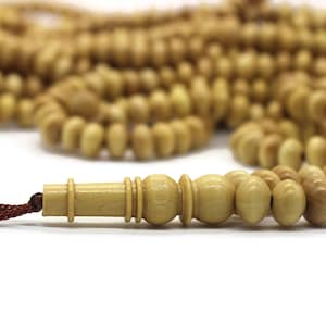 May include: A set of wooden prayer beads, or tasbihs, with a brown cord and a wooden tassel. The beads are light brown and have a smooth, polished finish.