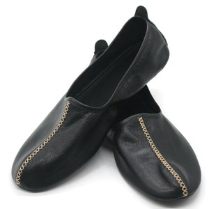 Puede incluir: Par de zapatillas de cuero negro con costuras doradas a los lados.