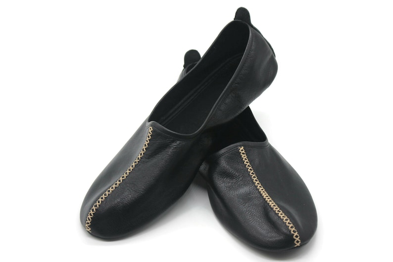 Puede incluir: Par de zapatillas de cuero negro con costuras doradas a los lados.