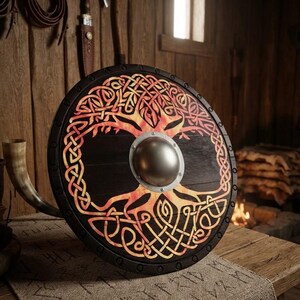 May include: A round wooden shield featuring a dark finish and a central metal boss. The surface displays a vibrant, fiery orange and yellow painted design of an intricate tree with interwoven Celtic knotwork branches and roots.