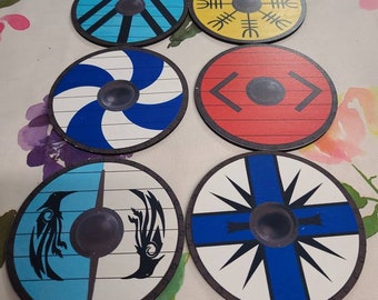 May include: Six round wooden shields with different designs. The shields are painted in various colors, including blue, red, yellow, white, and black. Each shield has a central black circle.