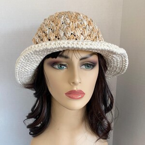 May include: A white crochet hat with a beige and white crocheted crown. The hat has a wide brim and is made with a textured stitch.