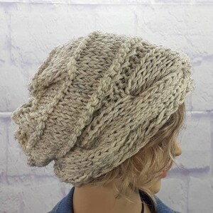 May include: A slouchy knit beanie hat in a light beige color with a cable knit pattern.