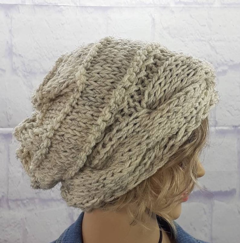 May include: A slouchy knit beanie hat in a light beige color with a cable knit pattern.