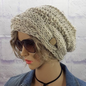 May include: A slouchy, light gray knitted beanie with a brown button detail. The beanie is made of a chunky yarn and has a relaxed fit.