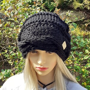 May include: Black knitted beanie with a slouchy fit and a small gold tag. The beanie is made of a thick, chunky yarn.