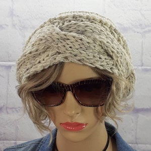 May include: A white knitted headband with a twisted design. The headband is worn by a mannequin with brown hair and sunglasses.