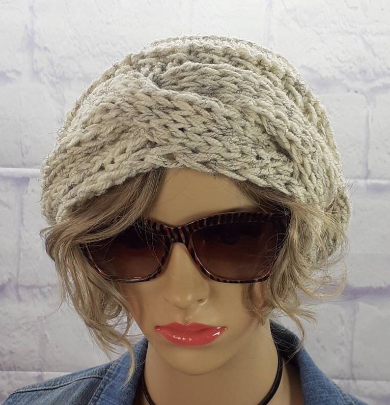 May include: A white knitted headband with a twisted design. The headband is worn by a mannequin with brown hair and sunglasses.