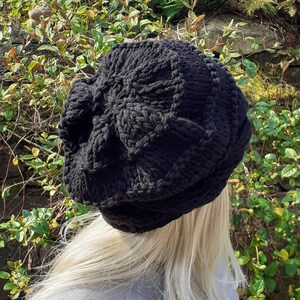 May include: A black knitted beanie with a textured pattern. The beanie is worn on a person's head.