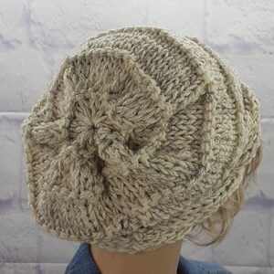 May include: A beige knitted beanie with a textured pattern. The beanie is made of a soft, fluffy yarn.