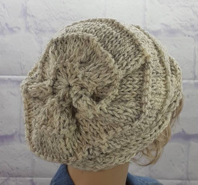 May include: A beige knitted beanie with a textured pattern. The beanie is made of a soft, fluffy yarn.