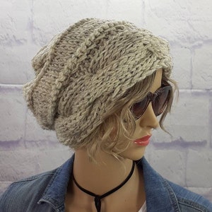May include: A beige knitted beanie with a cable knit pattern. The beanie is slouchy and has a folded brim.