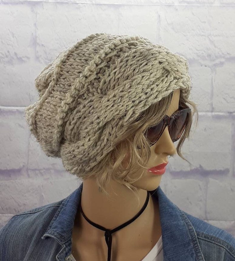 May include: A beige knitted beanie with a cable knit pattern. The beanie is slouchy and has a folded brim.
