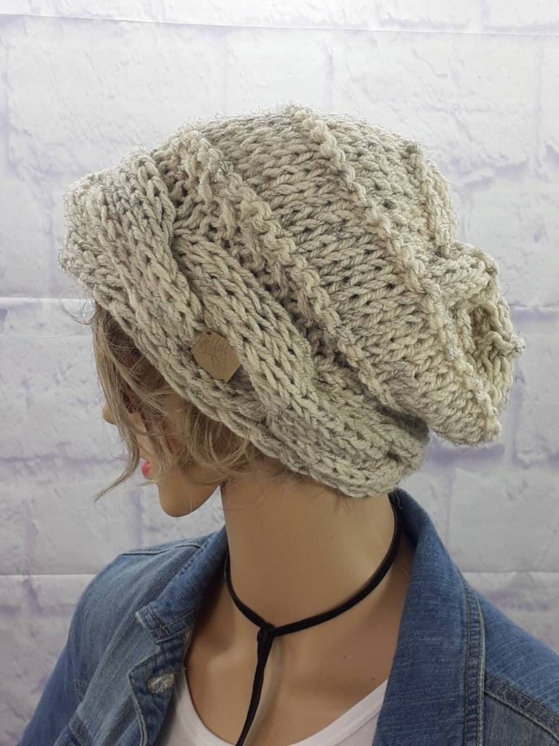 May include: A slouchy beige knitted beanie with a cable knit pattern and a small brown leather tag.