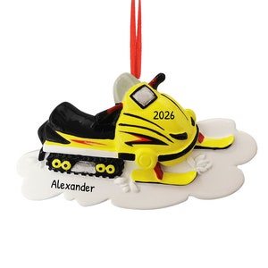 May include: Yellow and black snowmobile Christmas ornament with the year 2026 and the name Alexander on a white cloud.