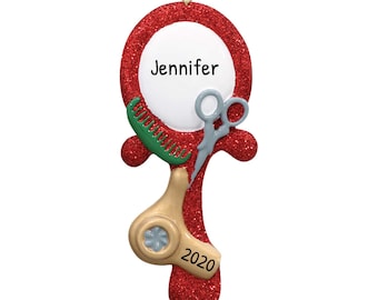 May include: A red glittery ornament shaped like a hand mirror, featuring a white circle with the name "Jennifer". It includes a green comb, gray scissors, and a tan hairdryer. The year "2020" is printed on the bottom. A gold loop is at the top.