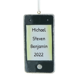 Könnte beinhalten: Ein silberner Glitzer-Weihnachtsbaumschmuck in Form eines Telefons mit einem schwarzen Bildschirm, auf dem die Namen Michael, Steven, Benjamin und das Jahr 2022 angezeigt werden.