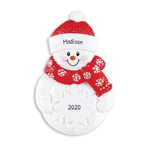 May include: White snowman Christmas ornament with a red hat, red scarf with white snowflakes, and a white snowflake with the year 2020. The snowman has a smiling face and the hat has the name Madison written on it.