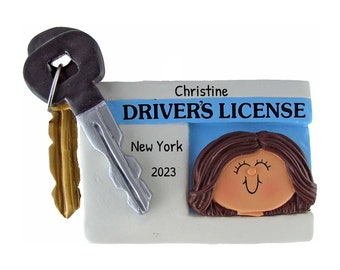 May include: A white and blue driver's license ornament with a cartoon woman's face, the text "DRIVER'S LICENSE", "New York", and "2023", and a key attached.